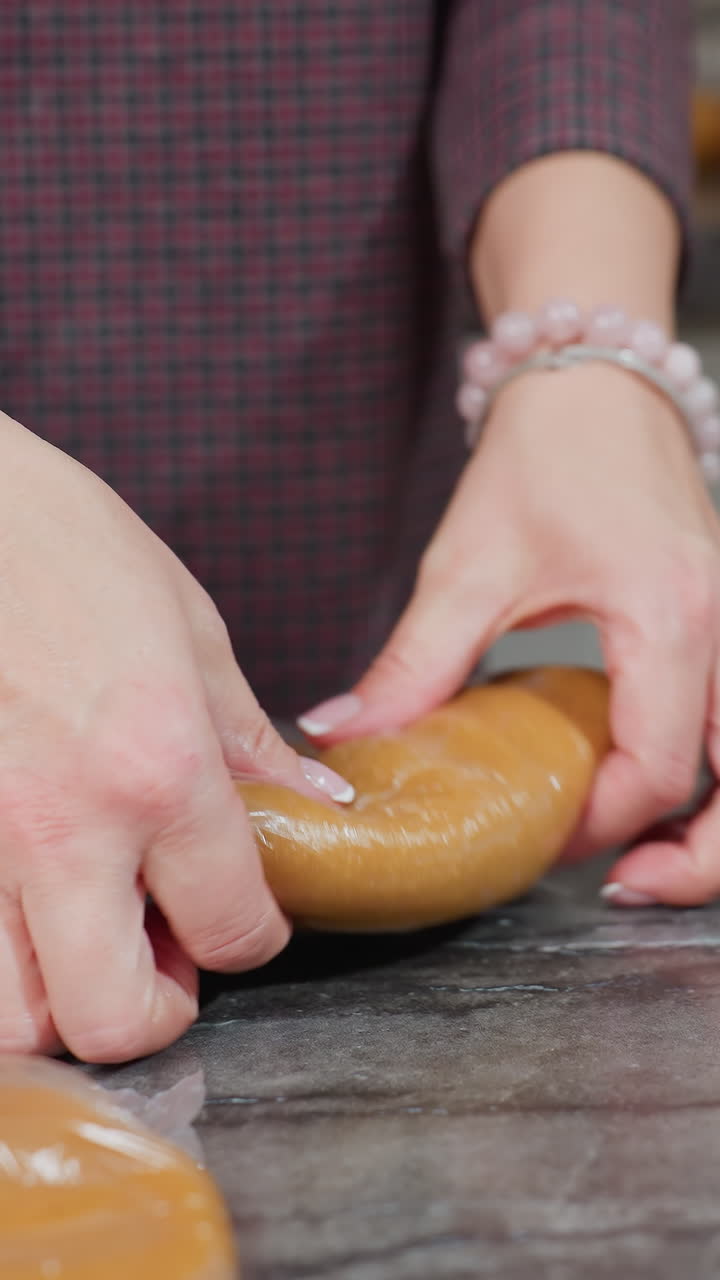 베이커는 주방 카운터에  가죽 포장 안에서 반죽을 압축하는 동안 다른 반죽이 근처에 머물고, 따뜻한 조명과 깨한 작업 공간으로 현대 주방 설정에서 베이킹을 준비합니다.