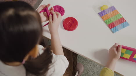 Top-View-Of-A-Little-Girl-Playing-With-Play-Dough-Sitting-At-Desk-In-A-Montessori-School