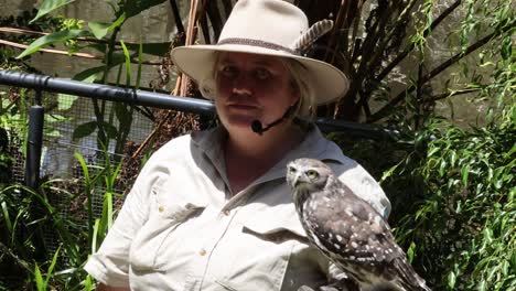 a woman in a hat holds and interacts with an owl