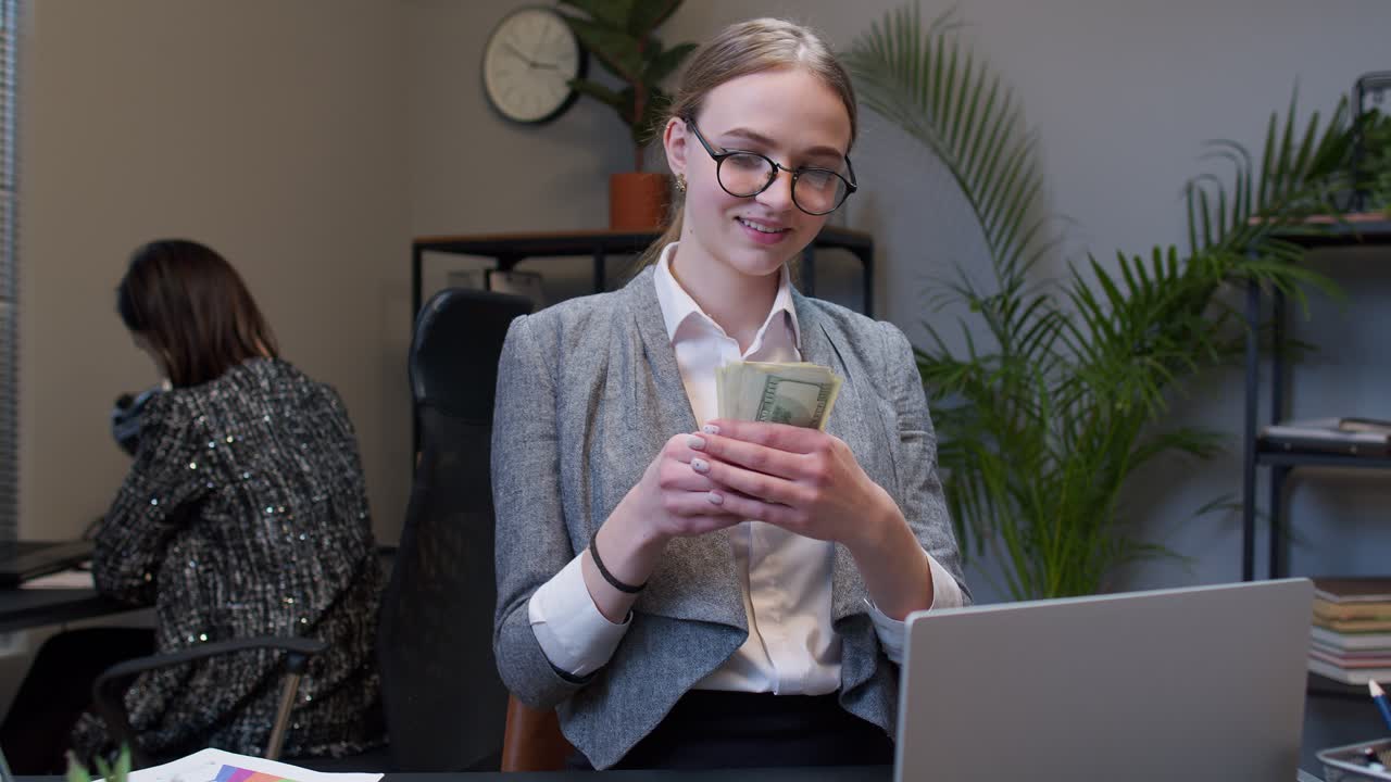 бизнесменка получает деньги наличные доходы от ноутбука в офисе после успешной финансовой сделки