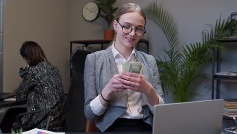 Businesswoman-receiving-money-cash-income-from-laptop-in-office-after-successful-financial-deal