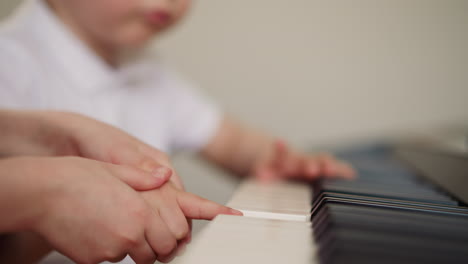 Girl-holds-toddler-boy-hand-and-presses-piano-keys