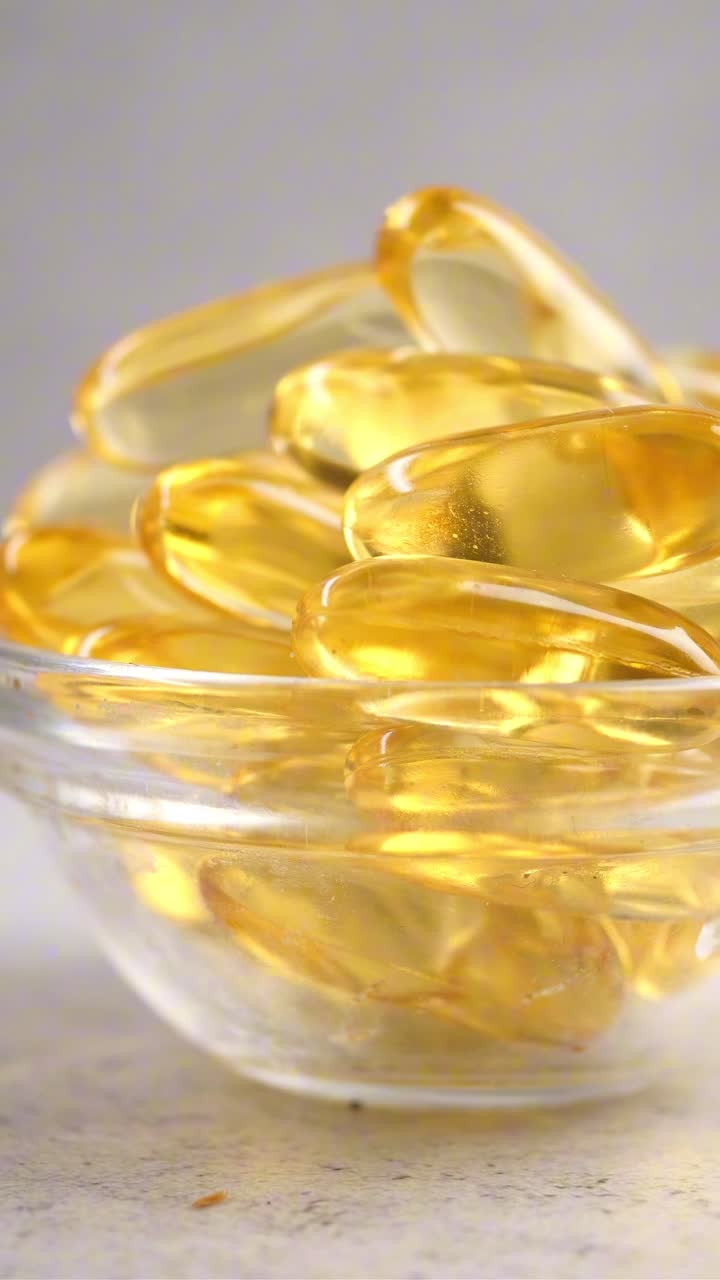 Potret dekat Kapsul Minyak Ikan Omega-3 Emas dalam Mangkuk Kaca.