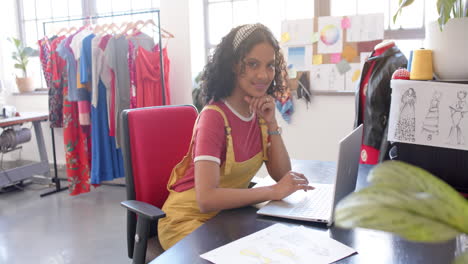 diseñadora de moda bi-racial feliz usando una computadora portátil en el escritorio en el estudio, cámara lenta