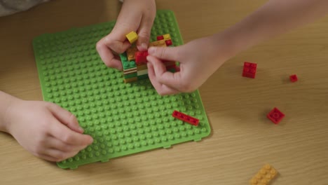 overhead shot of two children playing with plastic construction bricks on wooden table at home