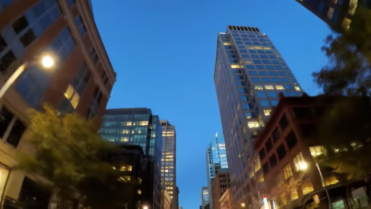 An evening stroll through a bustling city, showcasing towering buildings against a deep blue sky. The warm glow of lights creates an inviting atmosphere as night falls.