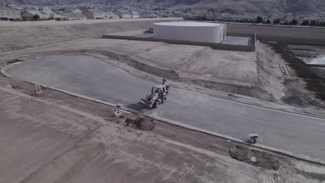 Un-Dron-Observa-Una-Retroexcavadora-Mientras-Deposita-Su-Carga-En-Un-Agujero-En-Un-Sitio-De-Construcción-De-Viviendas,-Preparando-El-Terreno-Para-Un-Mayor-Desarrollo