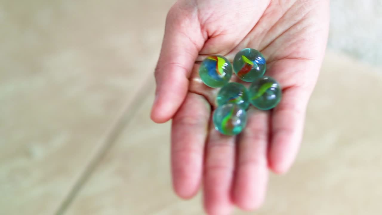 A hand showcases vibrant marbles against a tiled background, highlighting their glossy texture and vivid colors.