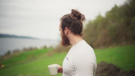 a bearded man drinking coffee outside with nature background