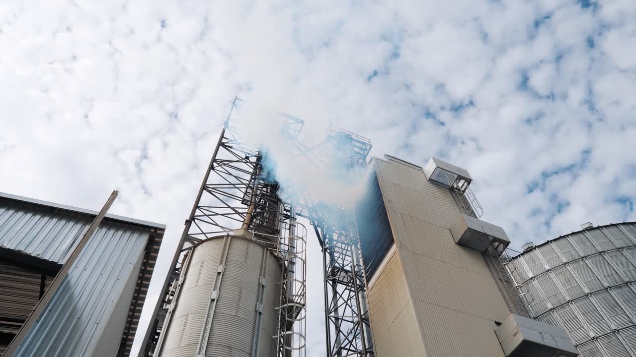 White smoke from industrial plant. Agricultural complex for grain storage. Vapor releases into the air from metal container for drying grains. Pollution the environment