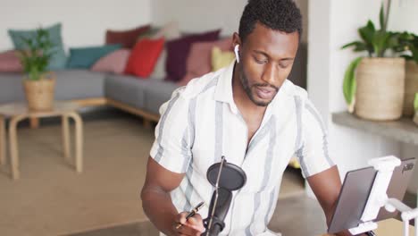 Happy-african-american-man-sitting-at-table-in-kitchen,-using-tablet-and-making-vlog