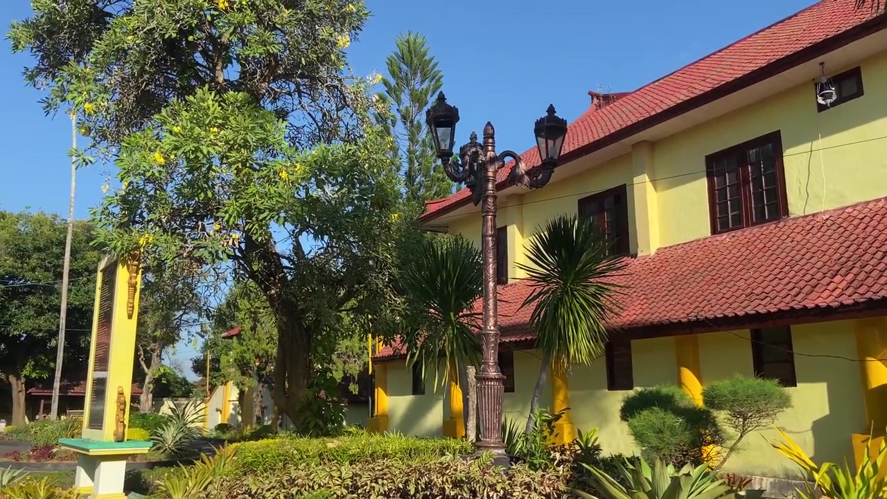 Bangunan Kuning Tradisional dengan Atap Merah dan Taman Tropis di Bawah Langit Biru