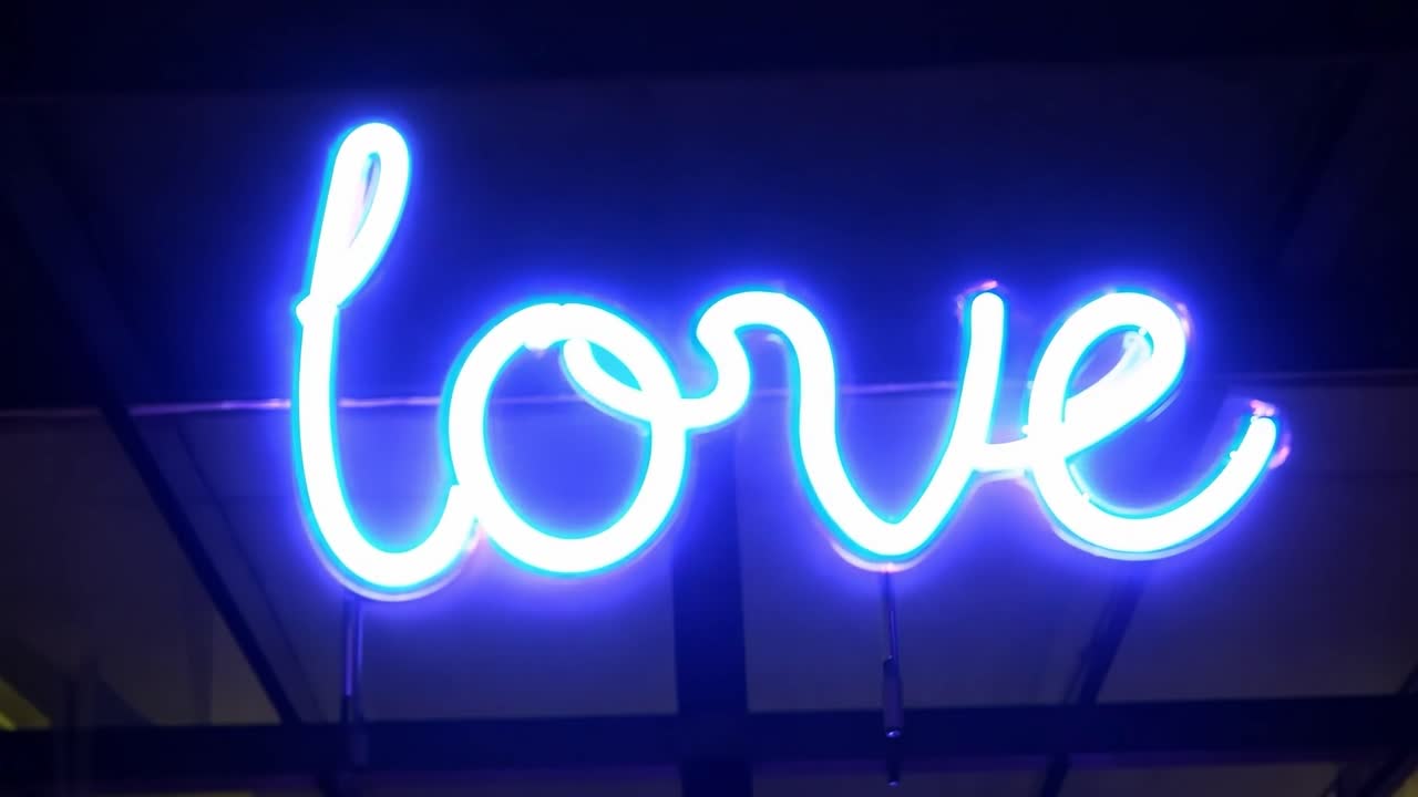 el letrero de neón azul y blanco parpadeante que muestra la palabra amor contra un llamativo fondo negro crea una atmósfera romántica