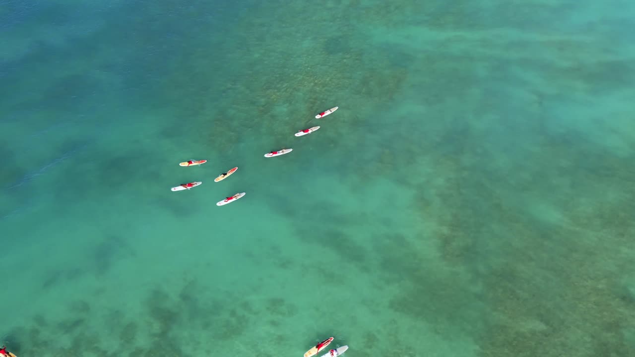Aerial shot of kayakers gliding through the clear shallow waters of Kailua Bay, Oahu, Hawaii. The calm blue water and stunning natural beauty provide a peaceful and scenic view