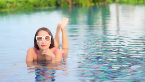happy exotic woman lying in shallow water of swimming pool, relaxing and enjoying on sunny summer day, full frame