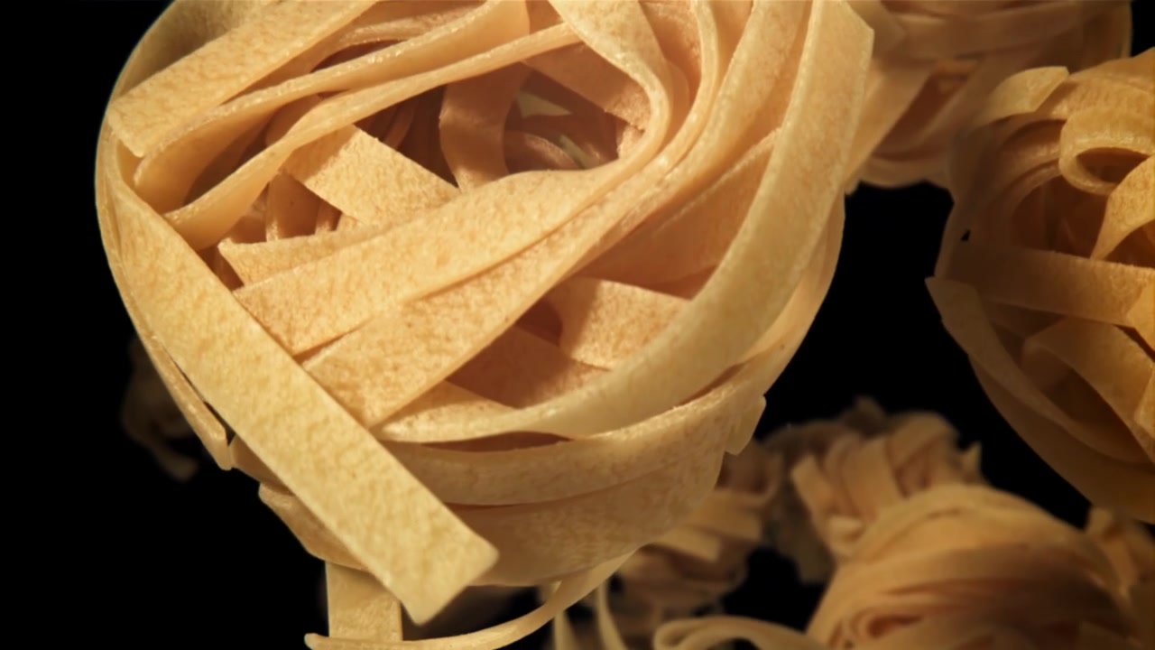 Nidi di pasta cruda che fluttuano verso l'alto su sfondo nero