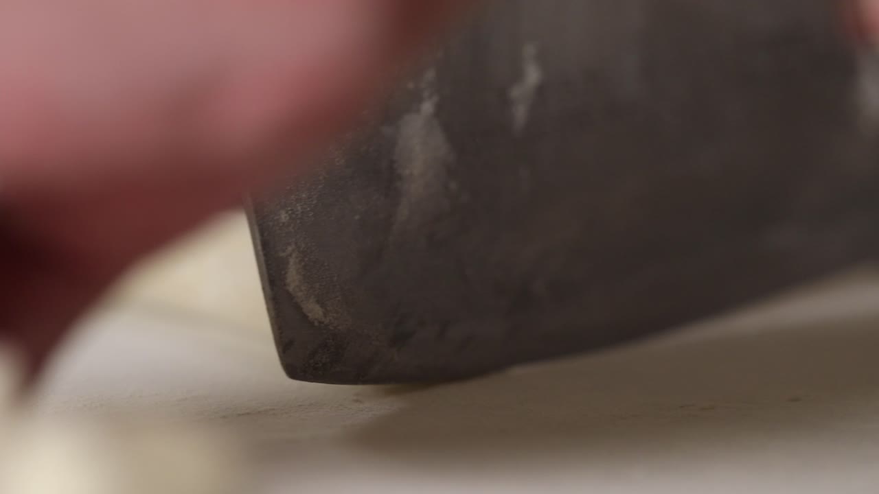 Extreme close up shot of a chef slicing a roll of dough for dumplings with a large kitchen knife
