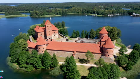 aerial: reveal shot of trakai island castle with green forest and blue color lake in the background