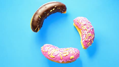 three donuts in the air, glazed in chocolate, pink, and yellow icing with sprinkles