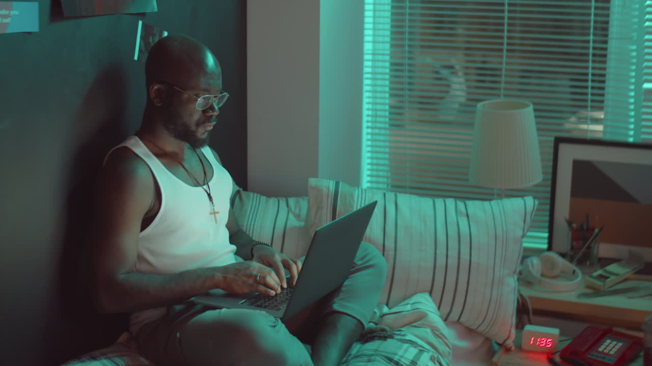 Black Man Using Laptop on Bed in Night