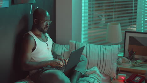 black man using laptop on bed in night
