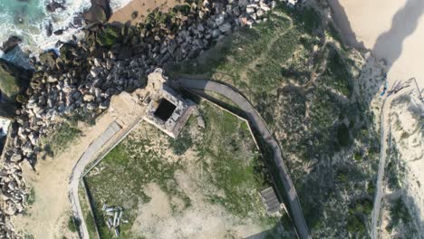 Aerial-view-of-the-ruins-of-an-old-lighthouse-by-the-sea-and-the-beach-on-a-sunny-day