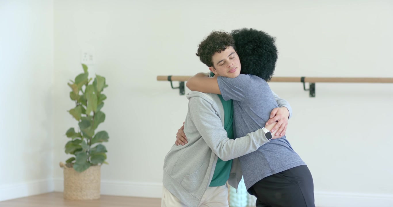 Diverse male partners initiating embrace stepping close kissing cheek holding by barre after class