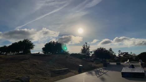 cielo azul, sol y nubes en movimiento, lapso de tiempo con algunos árboles avivados por el viento y algunos patinadores montando