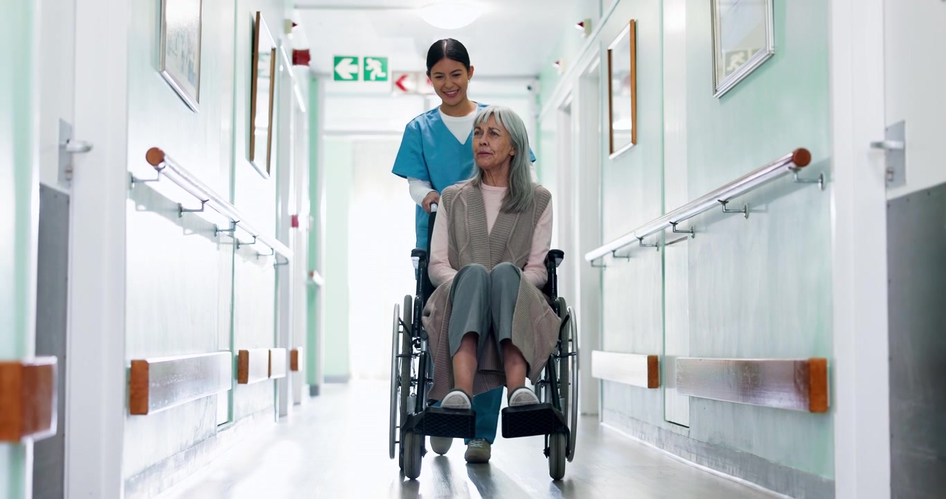 Nurse Pushing Senior Woman in Wheelchair Through Hospital Corridor