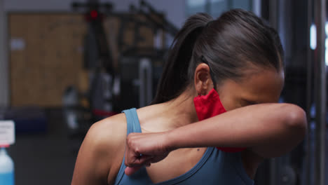 Mujer-Caucásica-En-Forma-Con-Mascarilla-Estornudando-En-El-Codo-En-El-Gimnasio