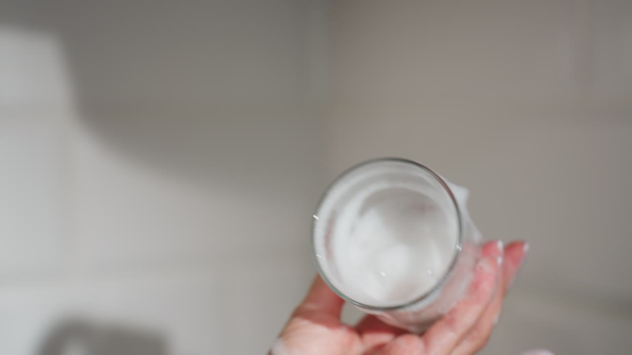 Close up hand view of person holding soapy glass cup covered in foam while cleaning carefully during dishwashing process in bright kitchen showing hygiene attention cleanliness care and neat routine