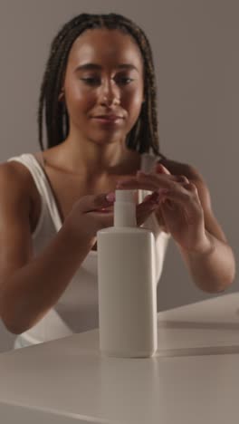 studio skincare beauty shot of woman dispensing moisturiser from bottle into hand