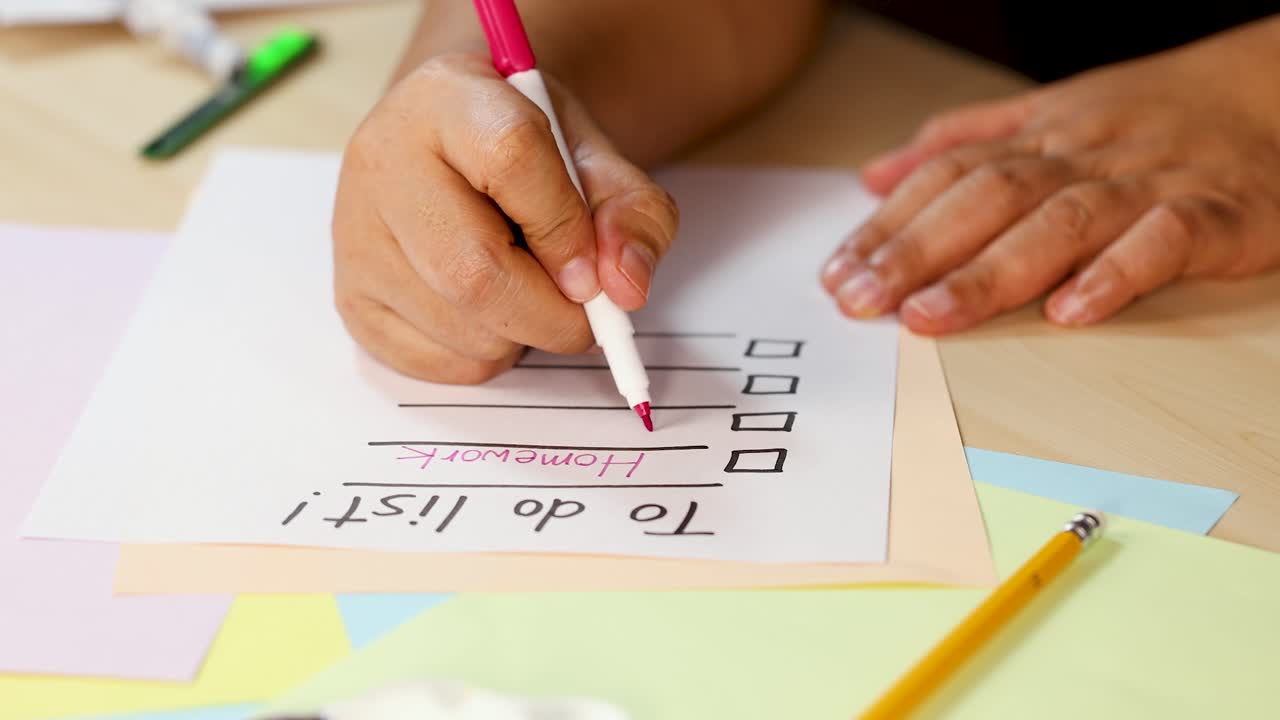 Person writes checklist on paper with marker, surrounded by stationery, in bright indoor lighting