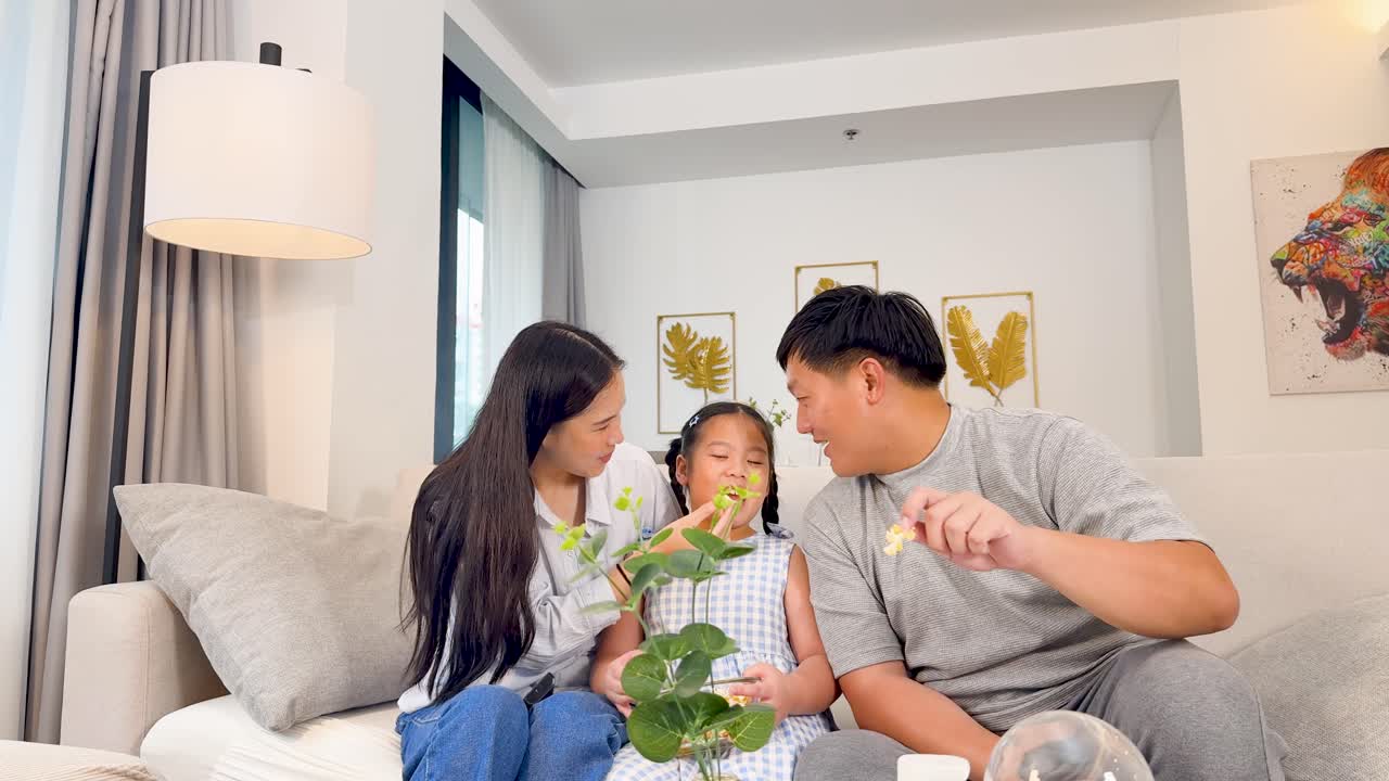 居心地の良いソファで、幸せなアジア人3人家族がポップコーンを食べながらテレビを見ている。