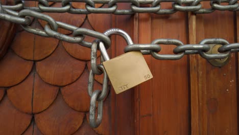 Track-in,-come-up-on-ornate-padlocked,-chained-wooden-door-on-a-bright-day