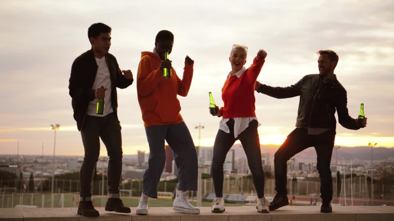 amigos multiétnicos bailando y bebiendo en un techo al caer la noche