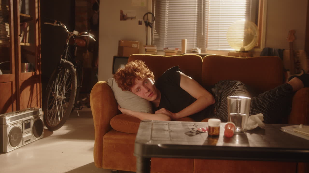 소파에 누워서 편안한 방에서 카메라를 바라보는 감정적으로 소진된 남자