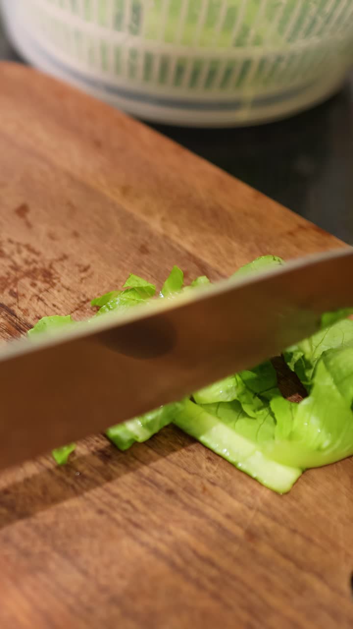 Ein Koch hackt mit einem scharfen Messer frischen grünen Salat auf einem Holzbrett