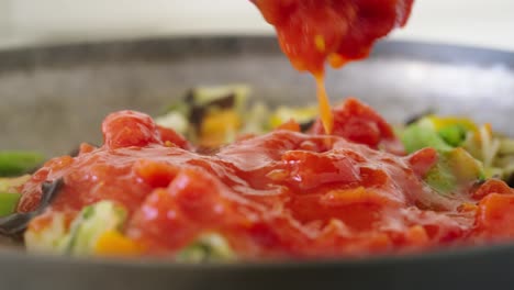 can of tomato sauce poured on top of steaming hot vegetables in a frying pan