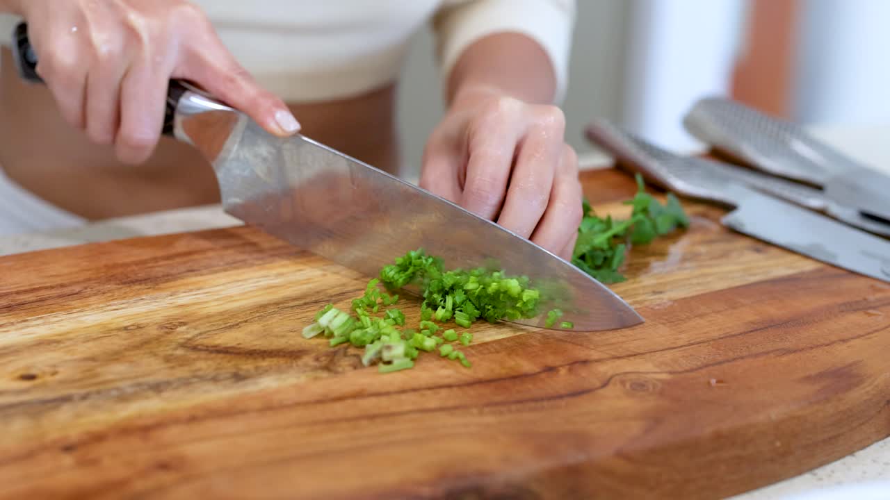 Close-up of hands skillfully chopping coriander on a wooden board with natural lighting