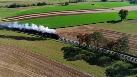 tren de pasajeros a vapor expulsando humo a lo largo de la campiña amish visto por un dron