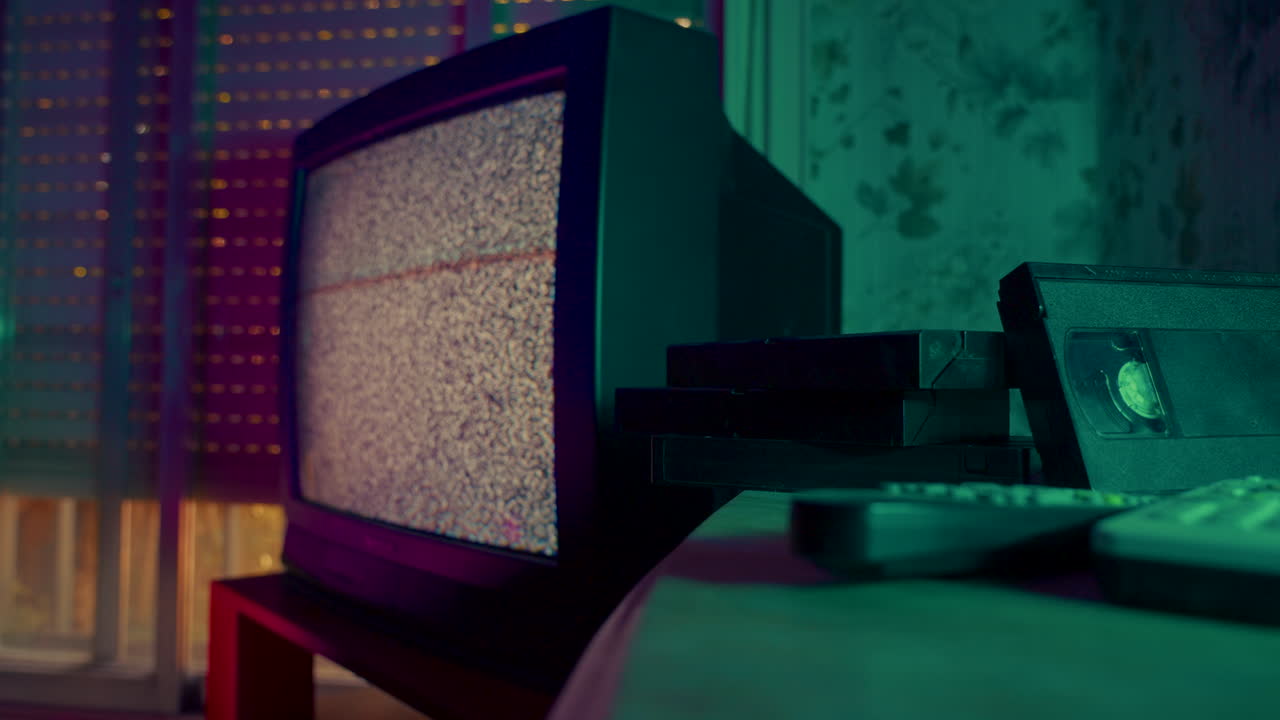 Televisione retrò con segnale disturbato e videocassette VHS in una stanza buia