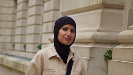 portrait of muslim businesswoman wearing hijab with modern business suit walking to work past city office buildings