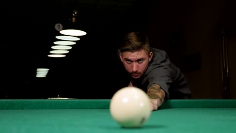 un hombre brutal con tatuajes en las manos está jugando al billar ruso en un bar.
