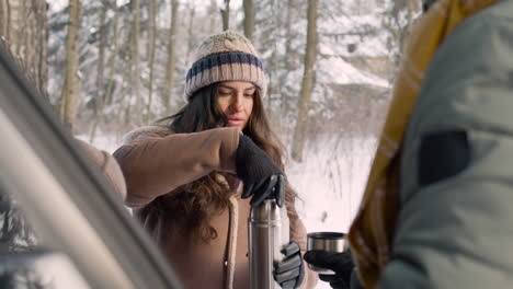 woman offers a hot drink from a thermos to her husband and daughter