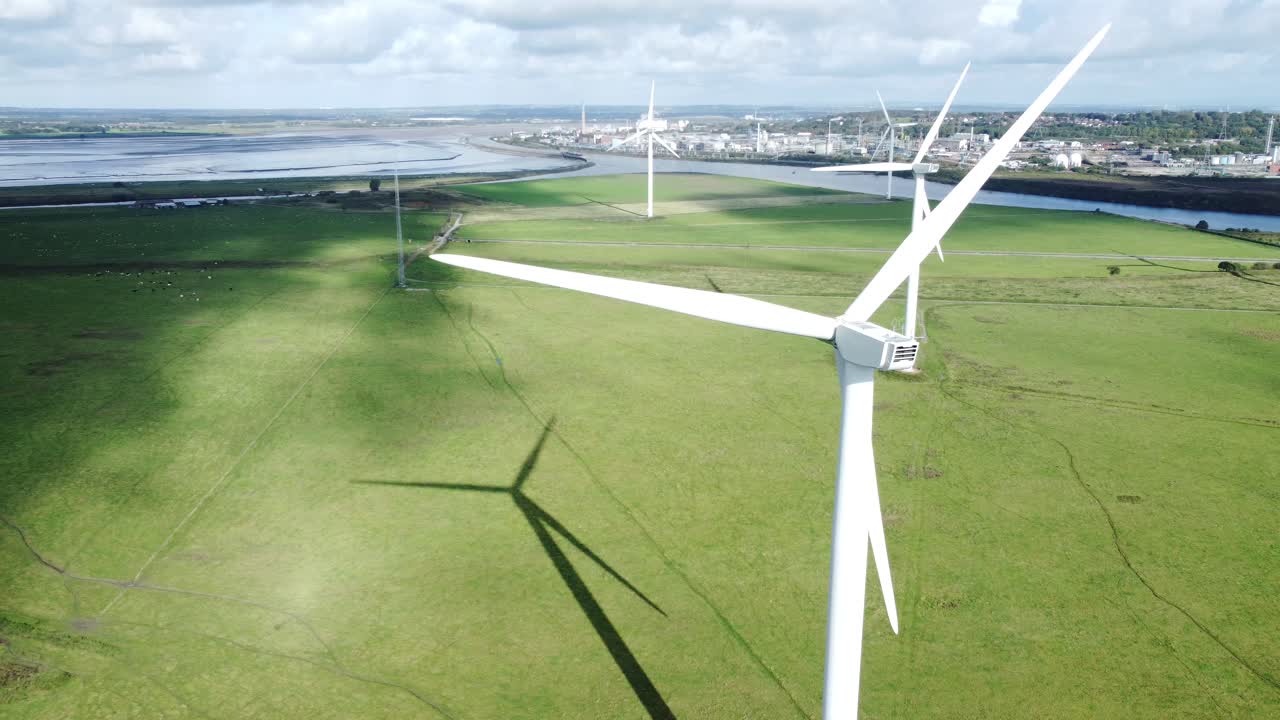 Aerial view flying around renewable energy wind farm wind turbines spinning on British countryside drifting right