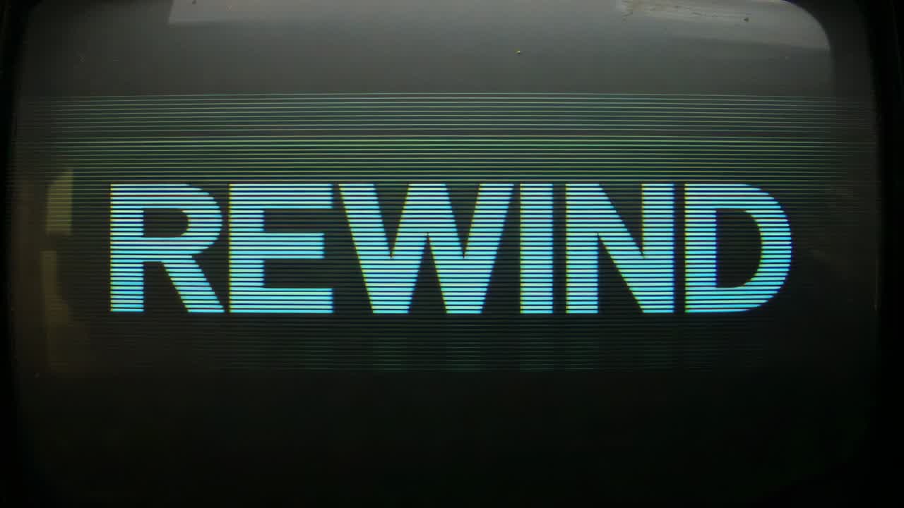 Displaying CRT monitor showing centered REWIND title in dark room, tape player initiating rewind