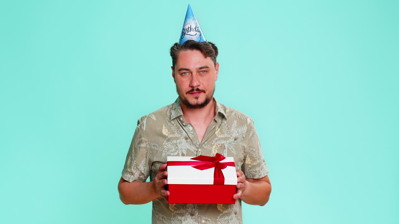 Hombre adulto con gorro de fiesta sonriendo alegremente mientras da un regalo de cumpleaños a alguien que celebra un evento con generosidad
