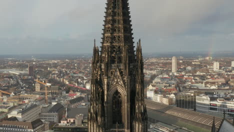 Dolly-shot-of-richly-ornamented-gothic-style-tower-of-Cathedral-Church-of-Saint-Peter-high-above-buildings-in-urban-borough.-Cologne,-Germany