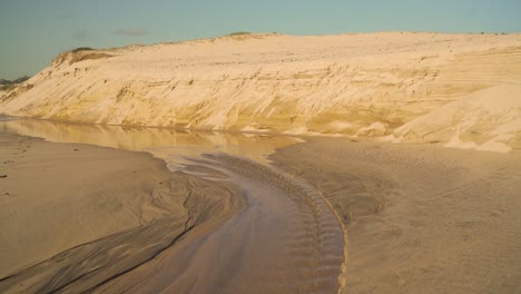 4k-Küstensanderosion-Am-Strand-Nach-Starkem-Regen,-Als-Wasser-Ihren-Weg-In-Den-Ozean-Bahnte